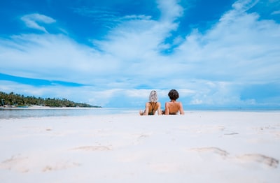 两个女人躺在白色沙滩上，面对蓝天下的海滩
